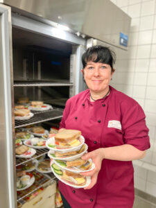 eine Köchin hält drei Teller mit Sandwiches