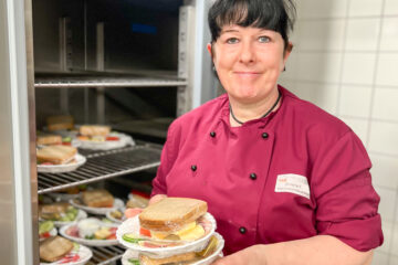 eine Köchin hält drei Teller mit Sandwiches